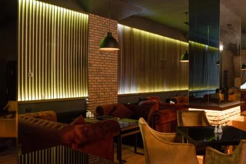 Dining restaurant with burgundy sofas and soft chairs in dim-lit Stock Photos
