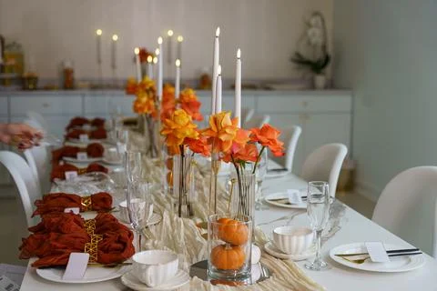 A dining table is arranged for a gathering with orange flowers, white candles Stock Photos