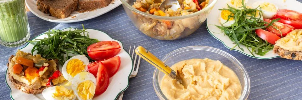 On a dining table, breakfast includes a boiled egg with arugula and tomato, h Stock Photos