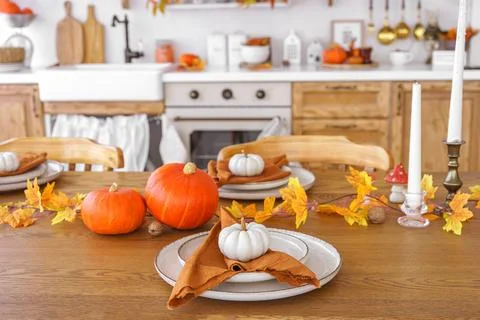Dining table decorated with pumpkins and fall foliage in a cozy kitchen set.. Stock Photos