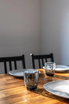 Dining table with glass and plates. Sunlit home table setting with copy space Stock Photos