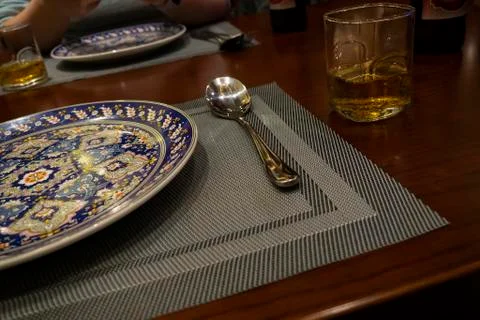 On the dining table is a plate with a pattern, a spoon and a glass of whiskey Stock Photos