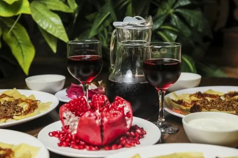 Dining table with red wine and pomegranate in a lush setting Stock Photos