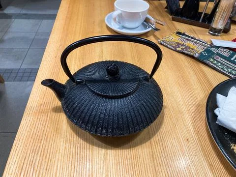 A dining table scene featuring a black teapot, food-filled plate, cup, bowl,  Stock Photos