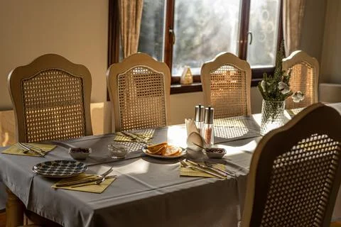 Dining table set with breakfast food wicker chairs and vase in bright sunligh Stock Photos