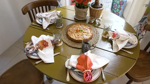 Dining table set with fruit tart, napkins, chairs, mugs, dishes and floral decor 库存影片 279270443