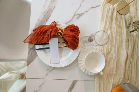 A dining table is set with a white plate, a red napkin, glassware, and a cup. Stock Photos