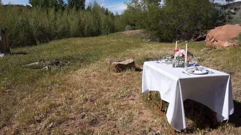 Dining table set in wilderness outdoor setting trees blowing Stock Footage 75023372