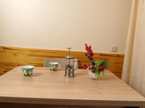 A dining table with two cups, a French press and a festive arrangement of ber Stock Photos