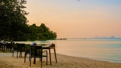 Dining tables standing on tropical beach at sunset, luxury resort Stock Photos