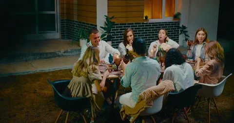 Dinner in backyard in summer evening, multiethnic group of friends enjoying Stock Footage 258511335