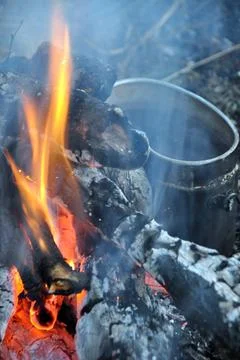 A dinner is being prepared at a forest campfire in a bowler hat. Stock Photos