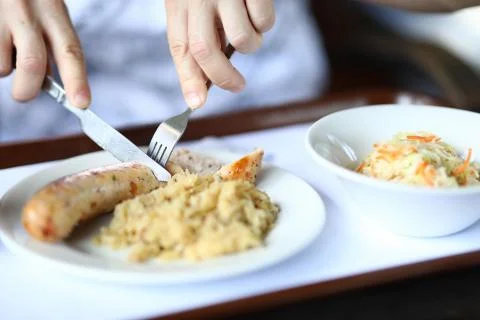 Dinner dish of stewed cabbage and salad sausages is on table visitor holds fork Stock Photos