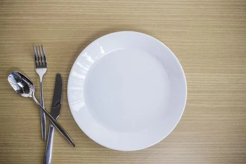 Dinner plate setting top view with knife, fork, white plate on a wooden table. Stock Photos