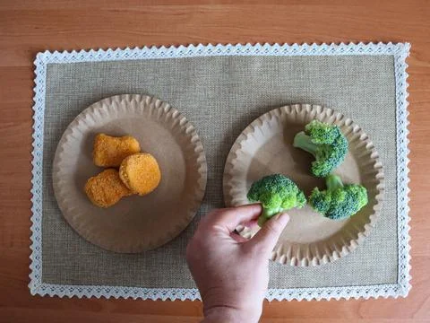 Dinner preparation includes broccoli and chicken nuggets on paper plates Stock Photos