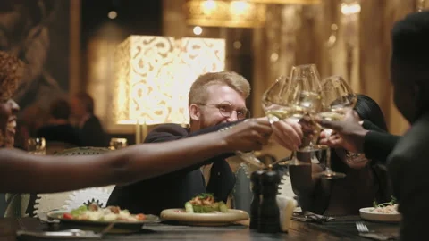 Dinner in restaurant in friday evening, group of multiethnic friends clinking Stock Footage 228183506