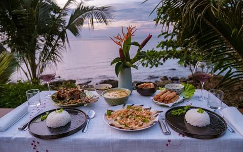 Dinner table looking out over ocean with Thai food, dinner during sunset Fotos Stock