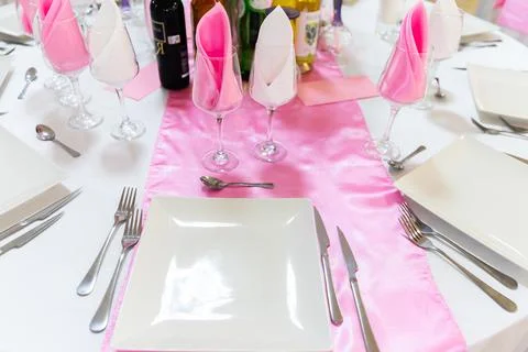 Dinner table setting with plates napkins glasses on pink satin runner caterin Stock Photos