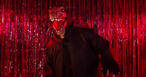 Dinosaur dragon mask in black cloak dancing at Halloween party, tinsel backdrop Stock Footage 337016096