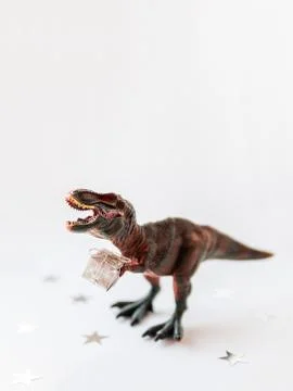 Dinosaur with present. Plastic toy with gift wrapped in silver paper. White b Stock Photos