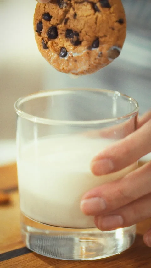 Dipping a chocolate chip cookie into milk for a cozy treat experience in day Stock Footage 331570059
