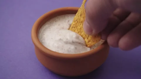 Dipping Corn Tortilla Chips into dip sauce  in purple bacground. Stockbeeldmateriaal 180024404