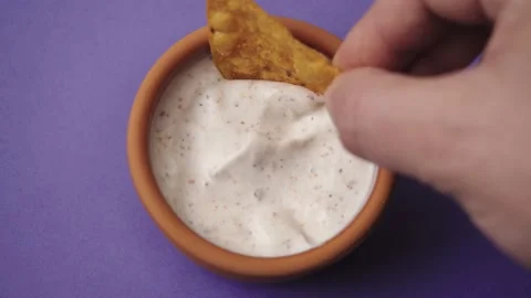 Dipping Corn Tortilla Chips into garlic dip sauce in purple bacground. Stockbeeldmateriaal 180025965