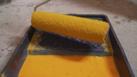 Dipping a paint roller into a tray with vibrant yellow paint for home Stock Footage 345537189