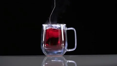 Dipping red tea bag in a transparent mug with hot water on black background Video stock 144431197
