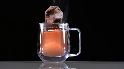 Dipping red tea bag in a transparent mug with hot water on black background Stock Footage 144431244