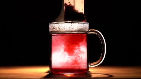 Dipping red tea bag in a transparent mug with hot water on black background Stock Footage 144431506