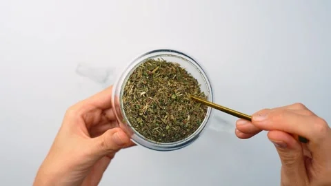 Dipping spoon in dry melissa leaves in glass jar. Top view, hands using yellow Stock Footage 342976372