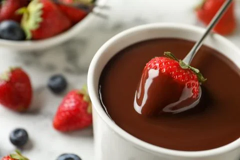 Dipping strawberry into fondue pot with chocolate, closeup Stock Photos