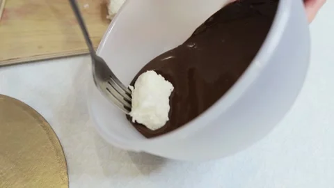 Dips a coconut candy on a fork in liquid chocolate Stock Footage 130231101