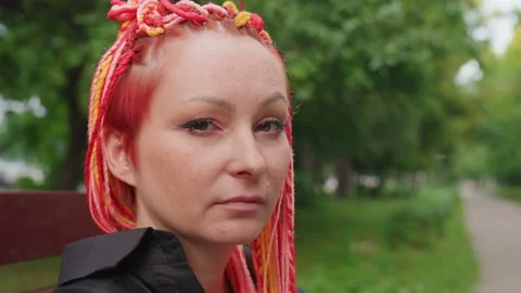 Direct closeup stare on bench caucasian woman with red braids meets camera with 库存影片 330718164