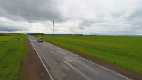 A direct highway in the middle of endless green fields  through which a car Stock Footage 119516573