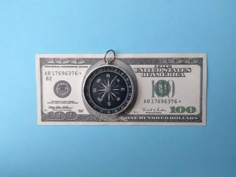 A directional pocket compass rests on top of a United States one hundred do.. Stock Photos