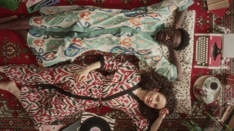 Directly Above of Smiling Young Couple in Robes Lying on Retro Rug 库存影片 339852707