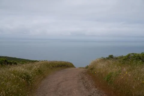 Dirt path dipping below view leading to ocean water, sense of unknown Stock Photos