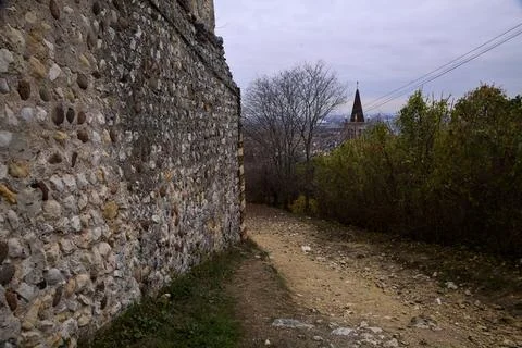 Dirt path on a hill next to an ancient wall and a bell tower in the distanc.. Stock Photos