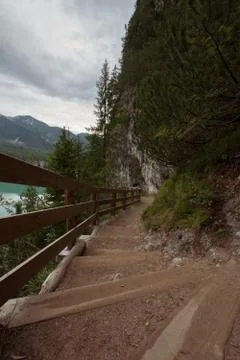 Dirt path to staircase runs along the Braies Lake under a cloudy sky Stock Photos