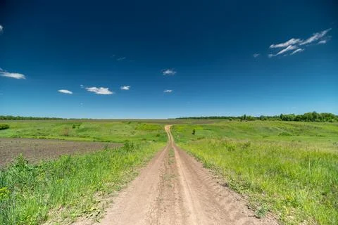 Dirt path through green summer fields under a clear blue sky Stock Photos