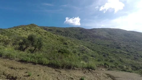 A dirt road between a mountain ridge on a sunny day with little passing clouds Video stock 148538717