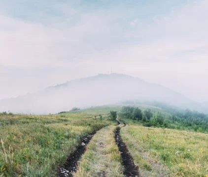 Dirt road in front of mountain covered by fog. Stock Photos