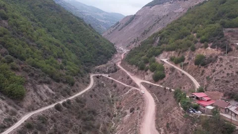 Dirt road leads through green hills toward hillside village with houses under Stock Footage 342705977