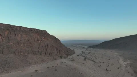 Dirt Road Through Desert Valley with Massive Cliff at Dusk Stock Footage 336025527