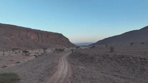 Dirt Road Through Desert Valley with Massive Cliff at Dusk Stock Footage 336025529