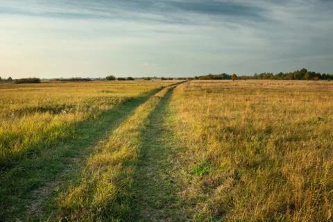 A dirt road through fallows and evening clouds in the sky Stock-Fotos