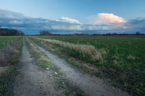 A dirt road through fields and clouds in the evening sky Stock Photos