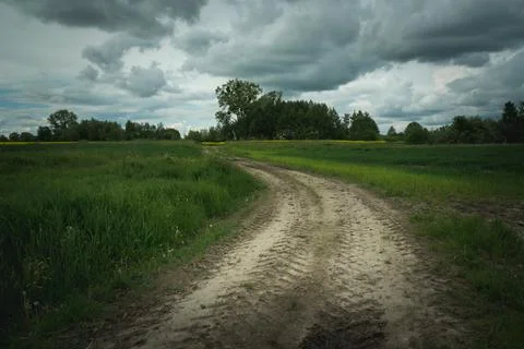Dirt road through fields and dark clouds Stock Photos